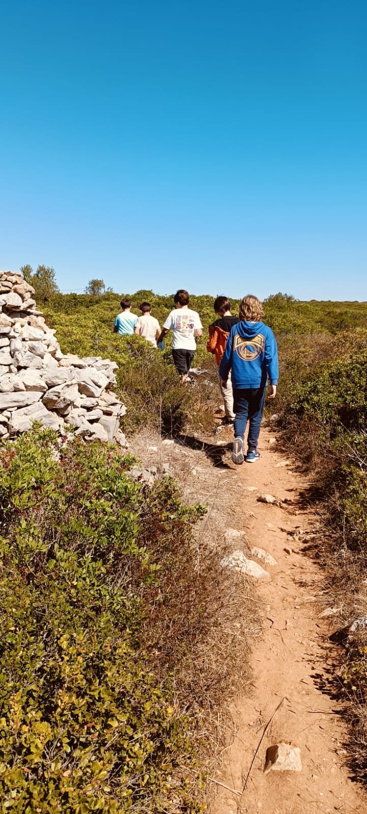Grupo a caminhar por trilho junto a uma ruína de pedra